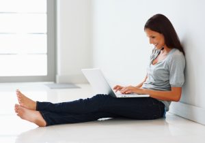 Pretty woman sitting against wall with laptop
